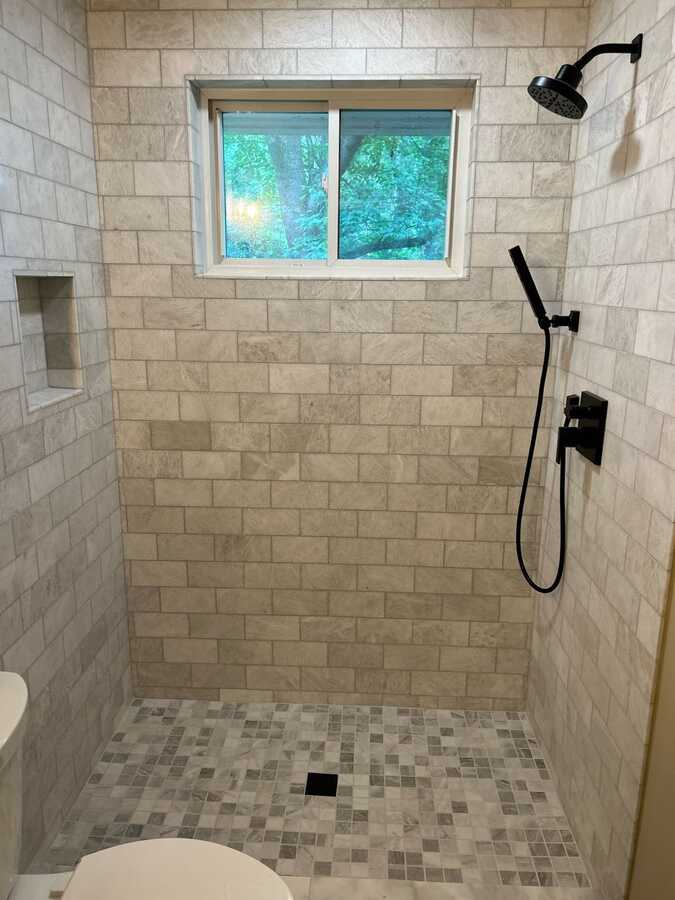 Tile shower wall with window, niche, and black shower fixture