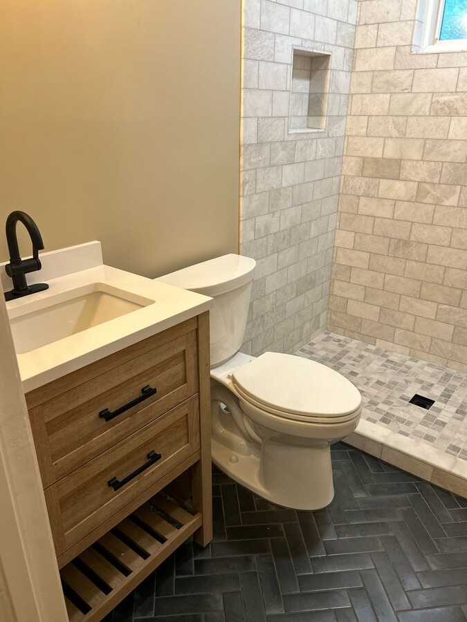 Bathroom vanity, black faucet, dark floor tile, and shower tile